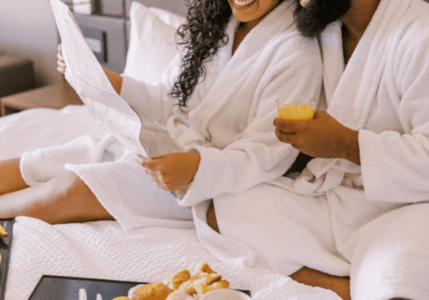 Happy couple having breakfast in bed wearing robes.